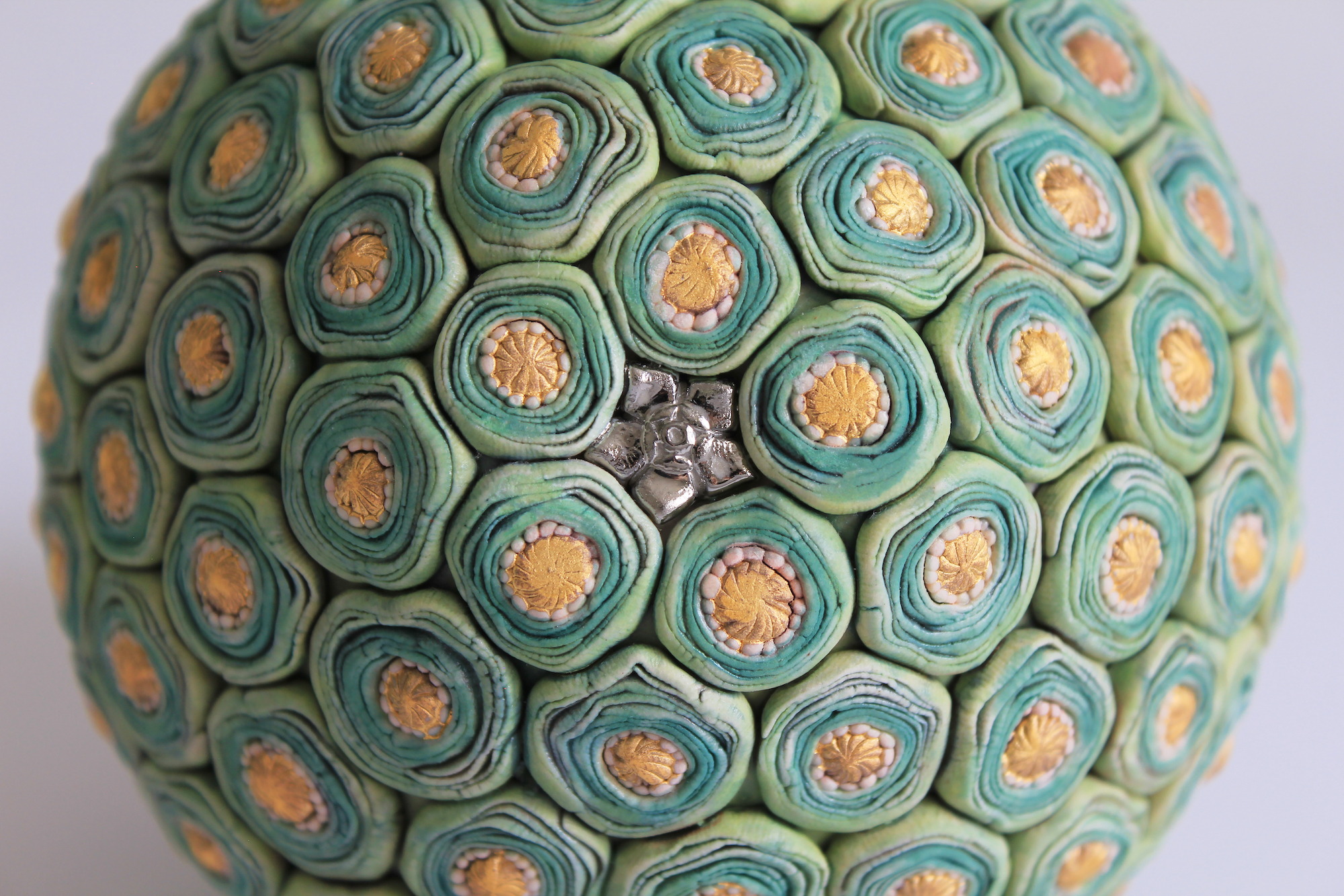 A detail of the base of a ceramic sculpture with details that resemble cut Brussels sprouts, tiny cabbages, or flowers.