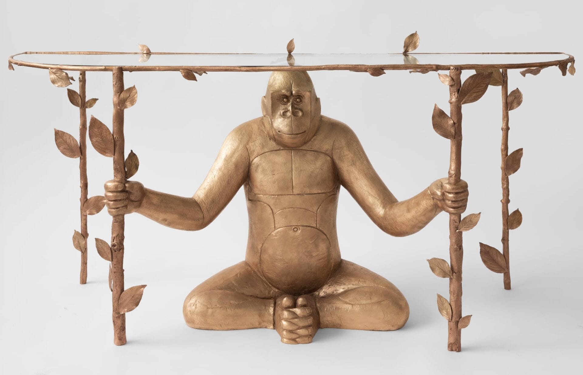 a tv console of a seated gorilla in bronze holding up twigs with leaves and a glass top 