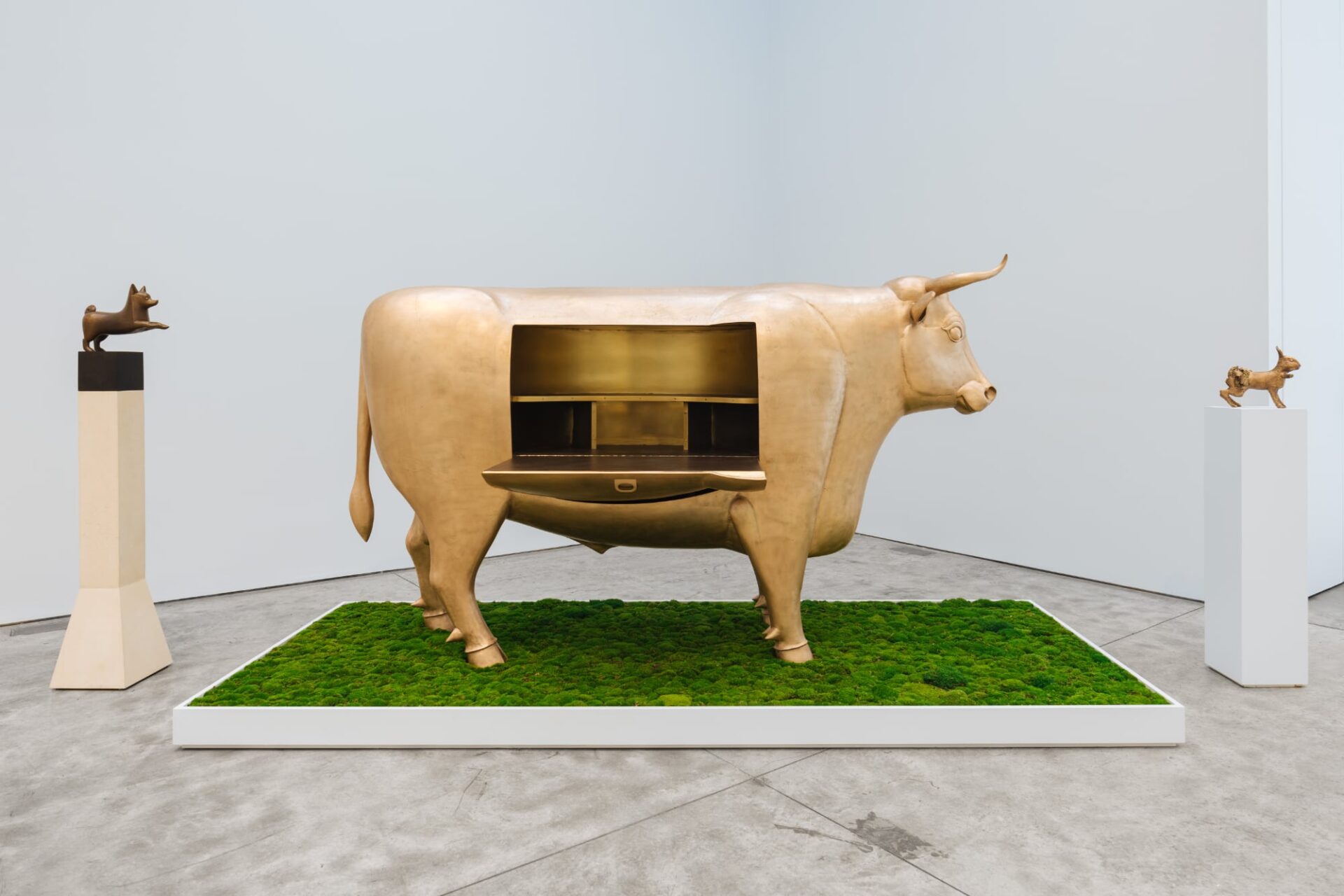 a cow sculpture that opens up like a desk with two small animal sculptures on pedestals on either side