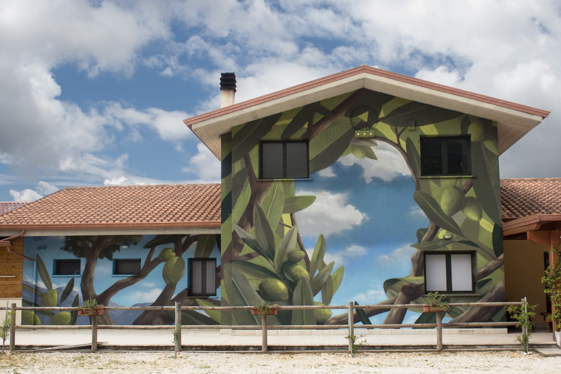 a mural of olive branches on the side of a building, which open up to reveal blue sky in the shape of a person's profile